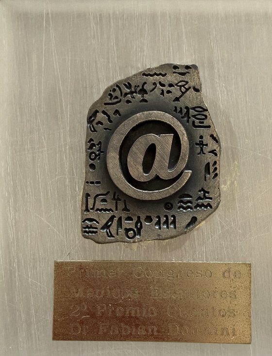 Trofeo del Primer Congreso Sudamericano de Médicos Escritores: placa de bronce con la inscripción «2º Premio Cuentos — Dr. Fabián Donnini» sobre una base de acrílico con un símbolo de arroba en relieve.